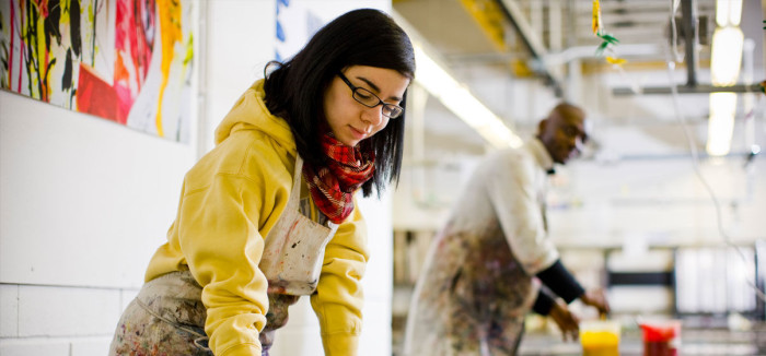 Two artists in overalls mixing paints in a large warehouse studio.