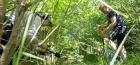 In the Swedish woods, a man is driving a spade into the ground while a woman bends down with a mic to capture the sound.