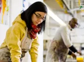 Two artists in overalls mixing paints in a large warehouse studio.