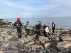 8 or so people standing on big stones at the edge of the sea.