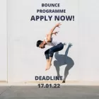 A male acrobat in jeans and a white vest jumps into the air.