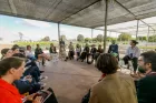 Group of around 30 people seated in a discussion circle, in what looks like a plant nursery, with rows of green plants behind them.