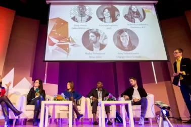 Photograph showing five seated contributors and one standing moderator on stage at a b.creative event.