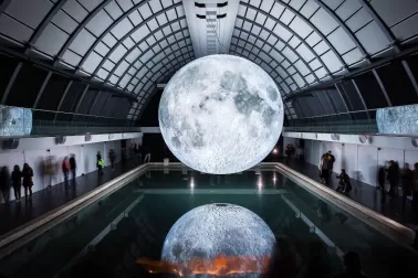 Photograph - a radiant moon hangs over a dark swimming hall, its luminous body reflected in the water.