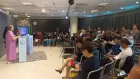 Arc of people sitting in the audience of the Cultural Mobility Forum 2022. Three speakers stand at the front behind boxy pedestals.