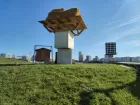 In a field on the outskirts of a city, a wooden platform has been built atop two large stacked crates - a kind of sky platform. Bales of hay rest atop it.