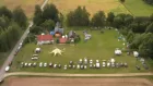 Aerial view of a field with some buildings and a line of parked cars.