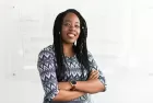 Stock image of a smiling woman standing with arms crossed in front of a whiteboard on which strategic notes are faintly visible.