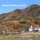 Toji Cultural Centre - a rectangular white building with red clay roof sitting at the base of a hill covered in green, golden and rust-coloured trees.